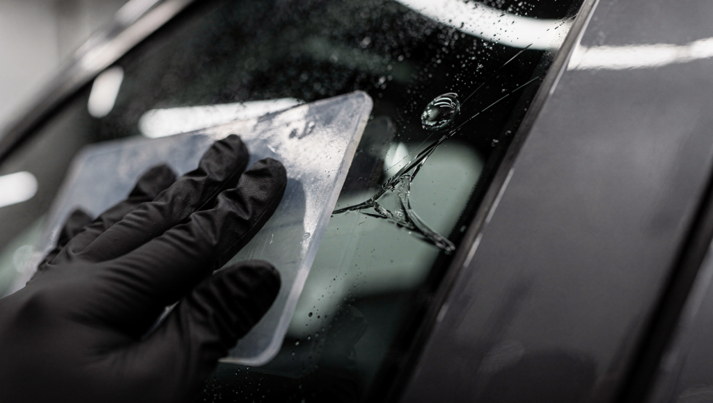 Installer using a squeegee to work an air bubble and crease out of dark window tint film