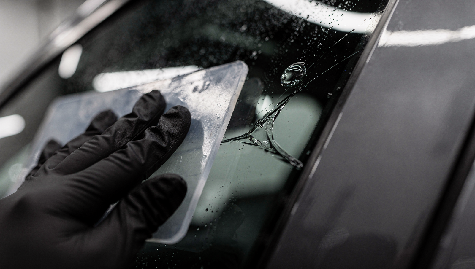Installer using a squeegee to work an air bubble and crease out of dark window tint film